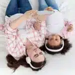 Mãe e filha deitadas juntas na cama usando fones de ouvido e olhando para celular, ouvindo música ou história para dormir