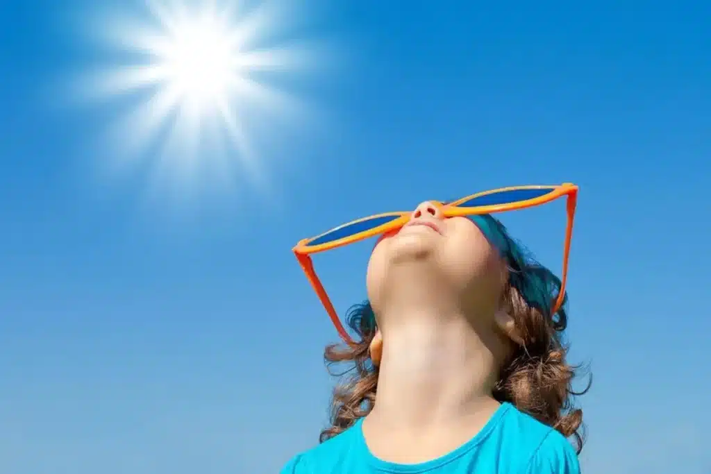 Criança olhando para o sol com óculos divertidos e camiseta azul