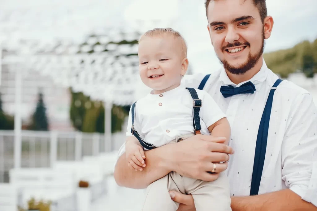 Padrinho sorridente segurando seu afilhado em uma cerimônia de batizado ao ar livre