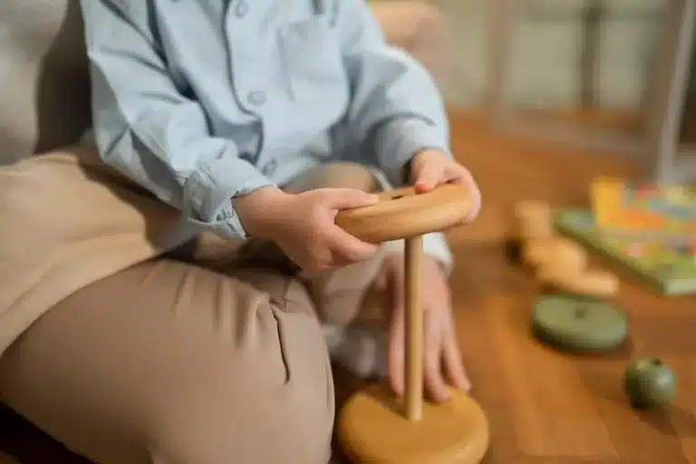 Criança brincando com brinquedo educativo de madeira no estilo Waldorf, desenvolvendo coordenação motora.