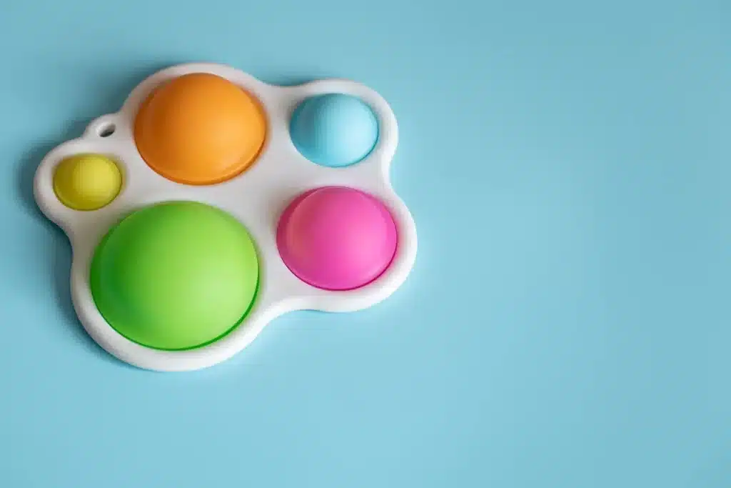 Brinquedo sensorial com bolhas coloridas em estrutura branca sobre fundo azul, usado para estímulo tátil infantil