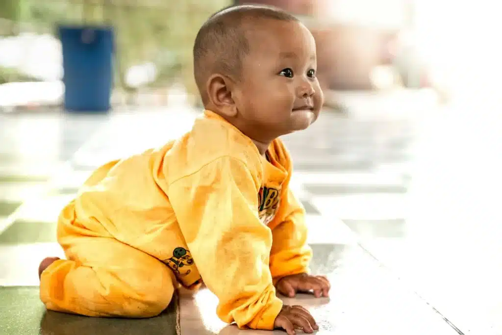 Bebê sorridente vestindo roupa amarela engatinha no chão, demonstrando uma etapa importante do desenvolvimento motor infantil.
