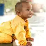 Bebê sorridente vestindo roupa amarela engatinha no chão, demonstrando uma etapa importante do desenvolvimento motor infantil.