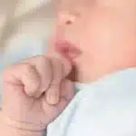 Bebê com bochechas avermelhadas e mão próxima à boca, possível sinal de brotoeja