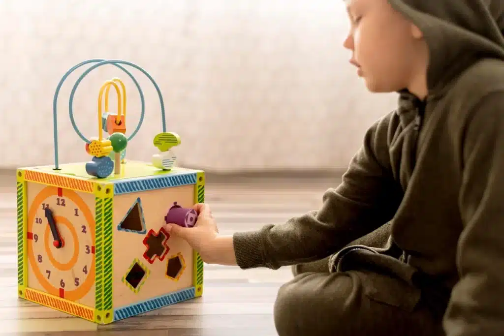 Criança brincando com uma caixa sensorial, colocando uma peça colorida em um dos compartimentos da caixa.