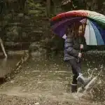 Menina com um guarda chuva brincando na água