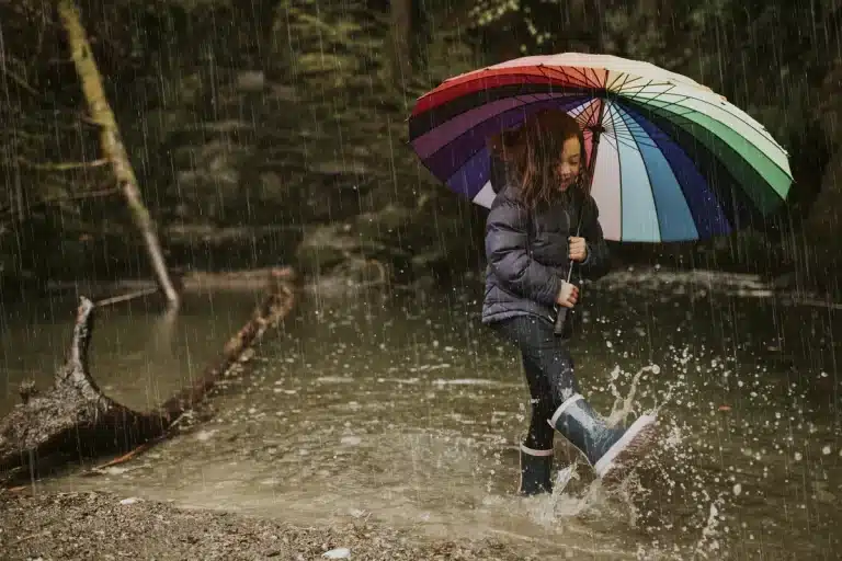 Menina com um guarda chuva brincando na água