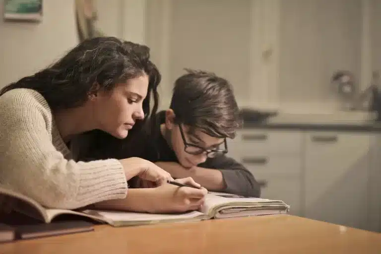 Uma menina ruiva escrevendo diligentemente em uma folha de atividades com um lápis, focada em aprender e praticar a caligrafia.