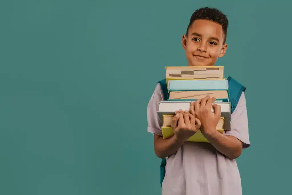 Menino sorridente com mochila segura uma pilha de livros contra fundo verde