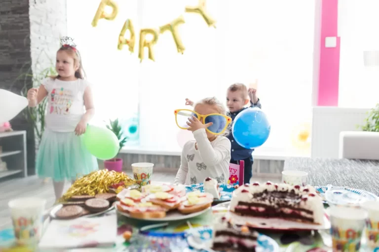 Crianças brincando e celebrando com bolo e balões em festa em casa infantil.
