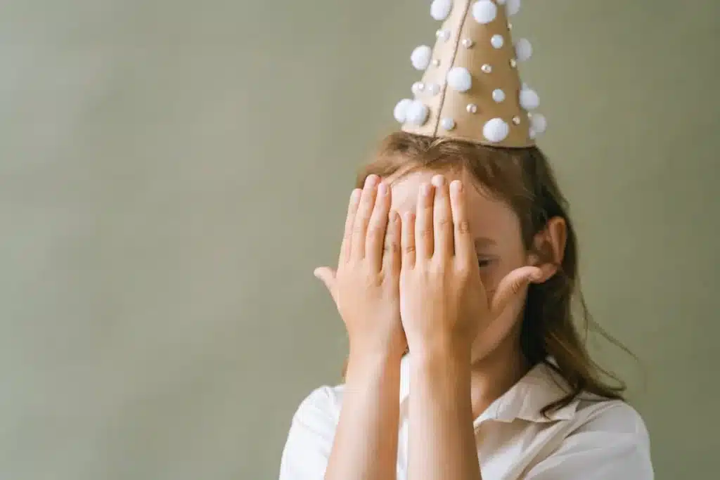Grupo de crianças com rostos pintados, deitadas na grama, expressando alegria em uma festa surpresa.