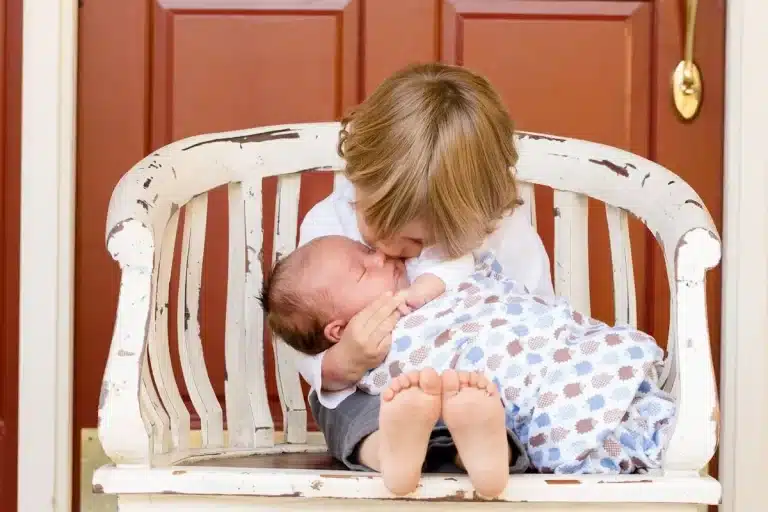 Criança mais velha beijando a cabeça do irmão bebê, em uma demonstração de amor ao próximo, carinho e afeto.
