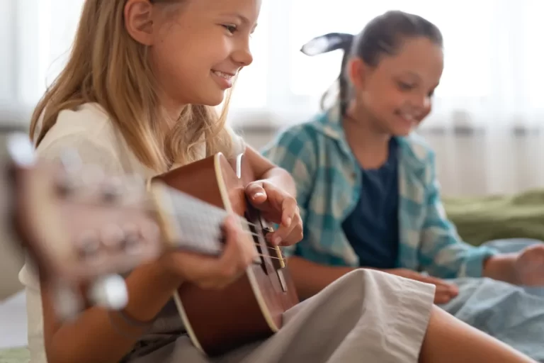 Duas meninas tocando ukulele, rindo e se divertindo juntas, em um momento de alegria com música de louvor.