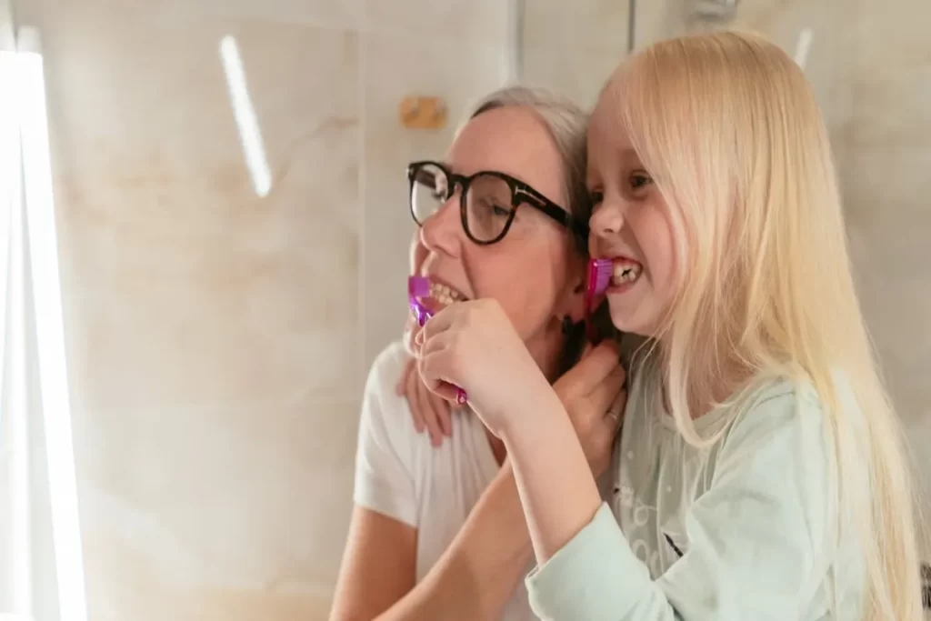 Avó e neta escovando os dentes juntas, reforçando a importância da higiene bucal para prevenir gengivite.