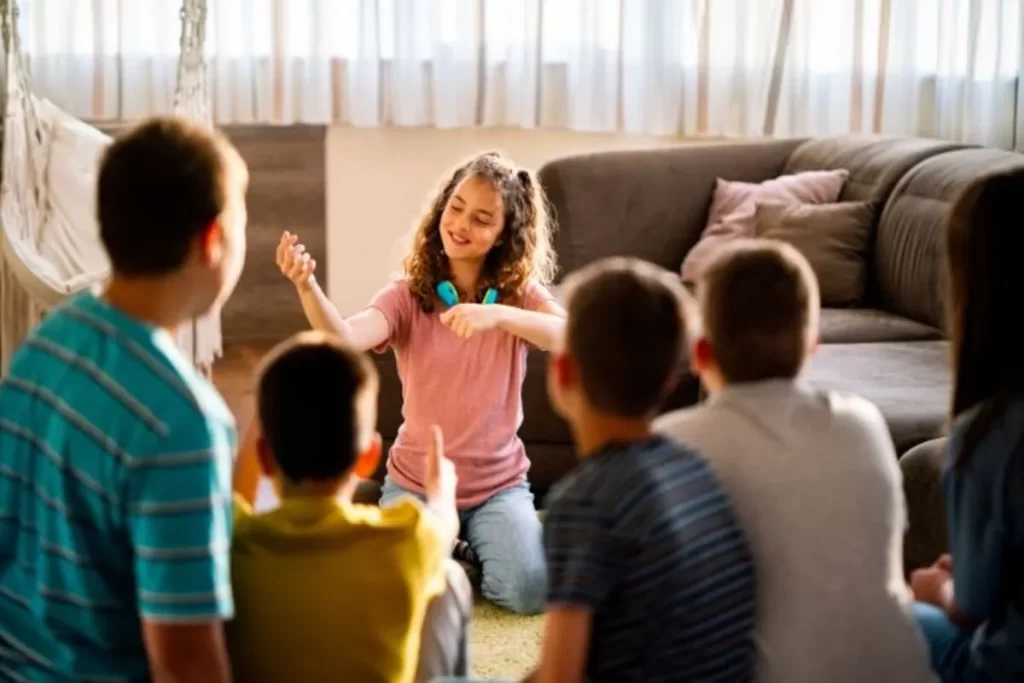 Menina fazendo mímica para um grupo de amigos sentados no chão da sala de estar.