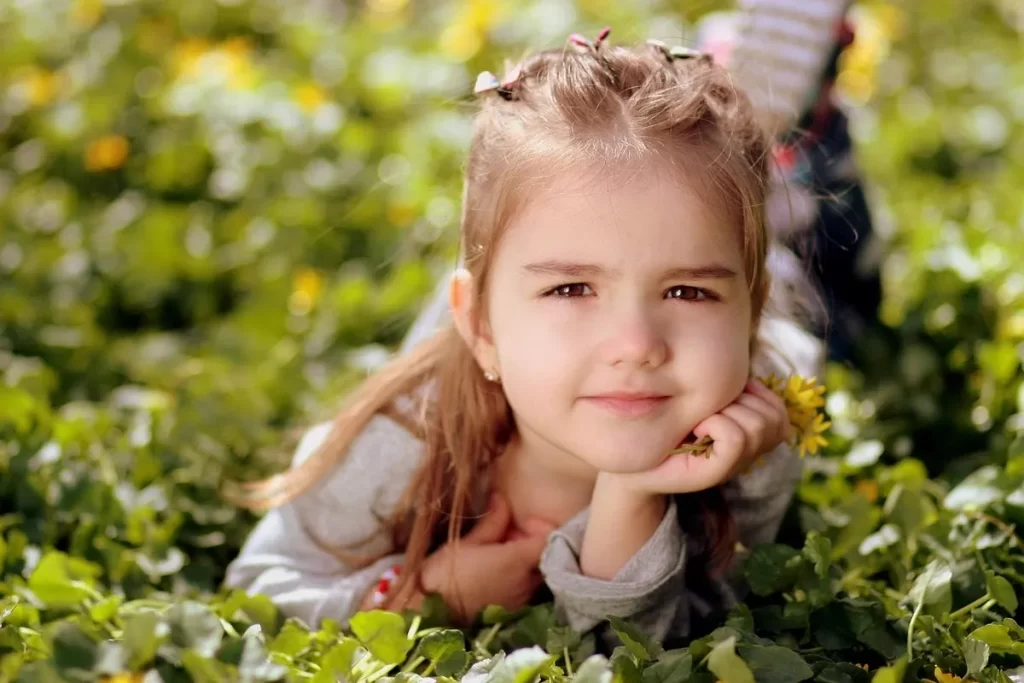 Menina com penteado floral deitada em um campo de flores, olhando para a câmera.
