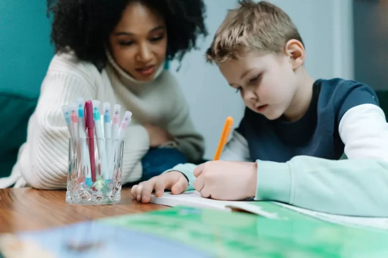Criança escrevendo com orientação de uma educadora, representando o processo de letramento e aprendizado da escrita