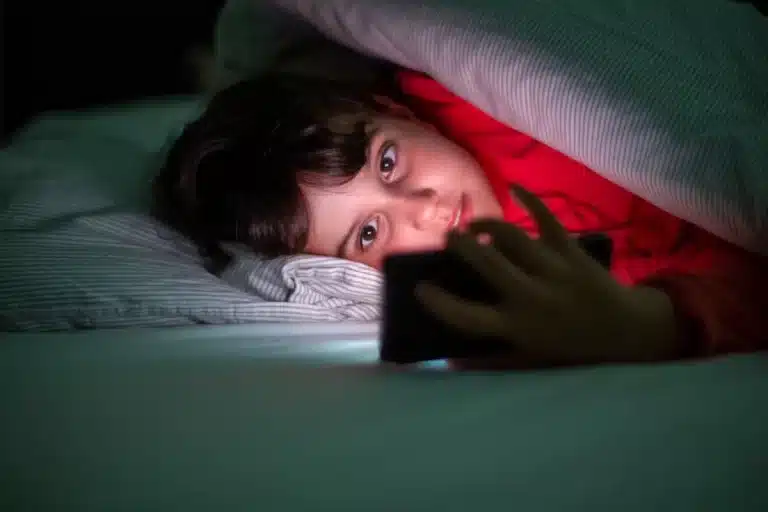 Criança deitada na cama usando o celular à noite, ilustrando os efeitos da nomofobia