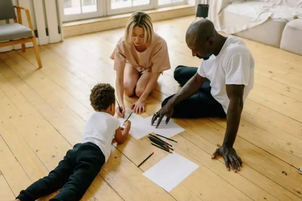 Pais sentados no chão ajudando o filho a desenhar, representando a prática da educação parental em casa