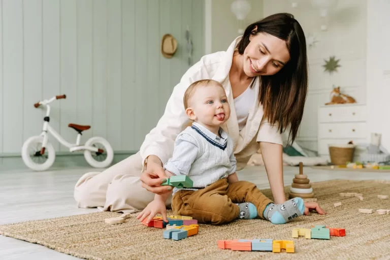 Mãe brincando com o bebê no tapete com blocos coloridos, estimulando a psicomotricidade infantil
