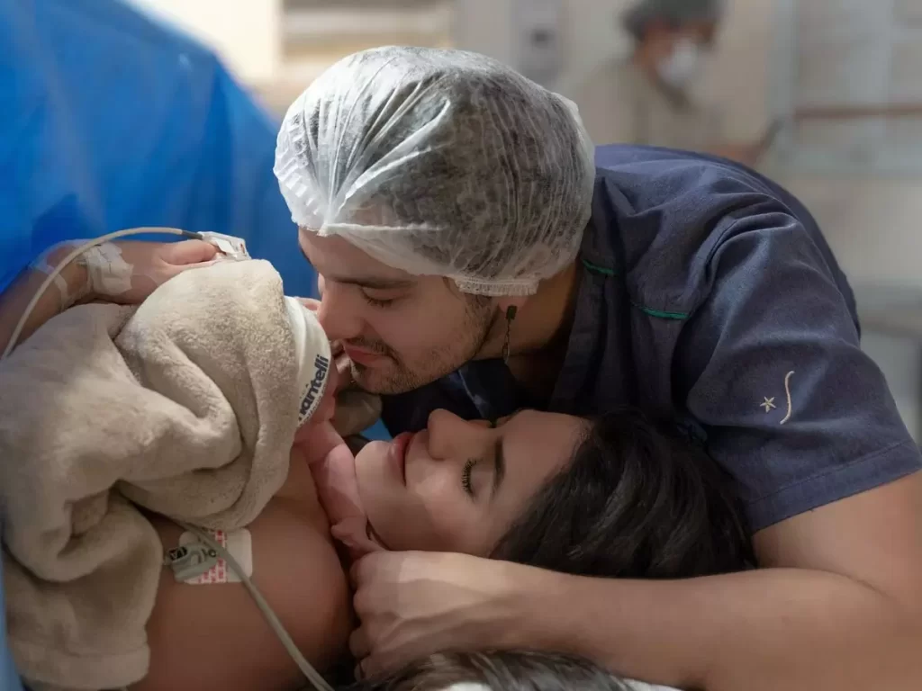 Luan Santana beijando a filha recém-nascida nos braços da mãe, logo após o parto, em um momento de ternura e emoção
