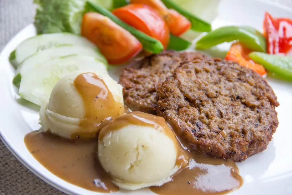 Prato com carne, purê e legumes frescos, representando alimentos ricos em ferro e refeições balanceadas