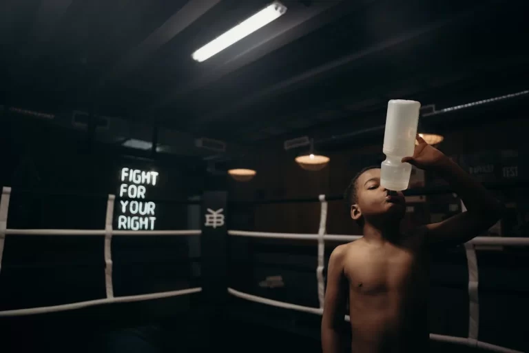 Criança tomando água dentro de um ringue de boxe, representando a importância da hidratação em academia para crianças