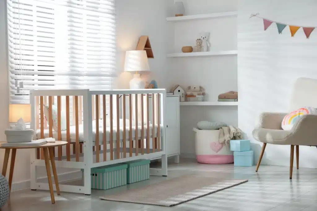 Quarto de bebê moderno com berço branco, iluminação natural e decoração minimalista em tons suaves.