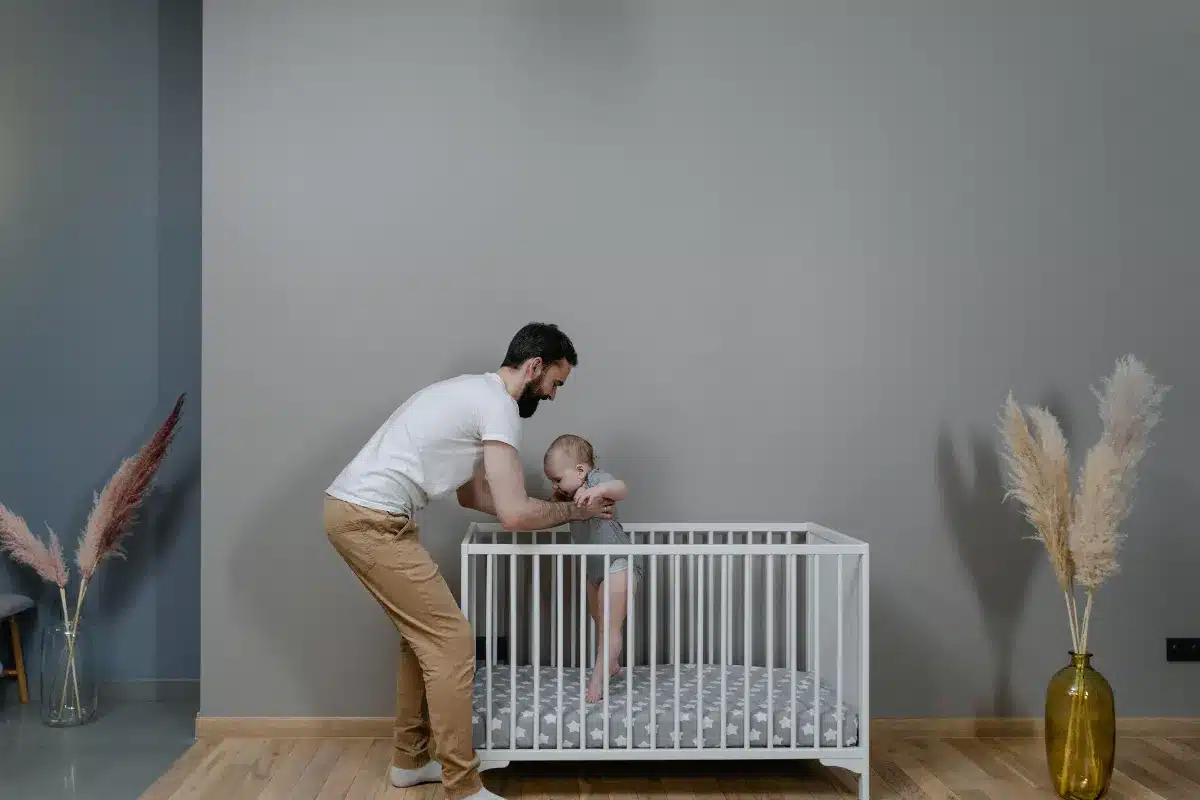 Pai colocando o bebê no berço em um quarto infantil