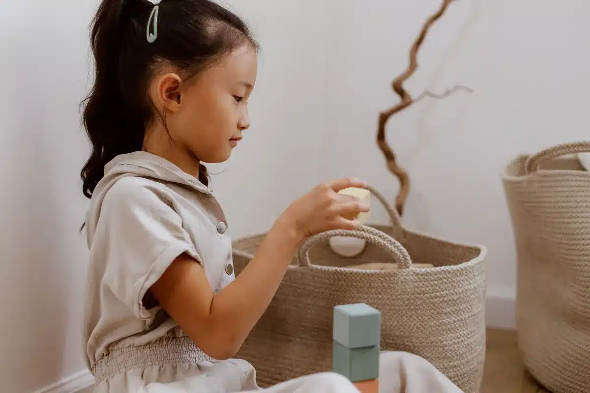 Menina guarda blocos em uma cesta durante a organização dos brinquedos