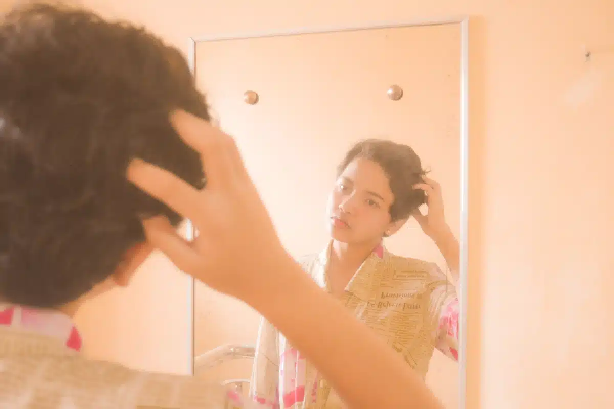 Adolescente observa o próprio reflexo no espelho enquanto ajeita o cabelo